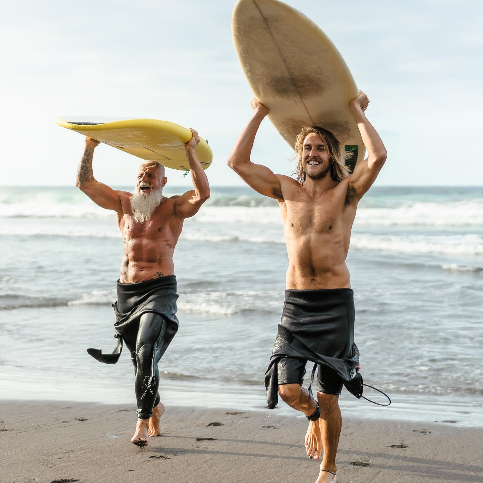 Two older men carrying surfboards on a beach